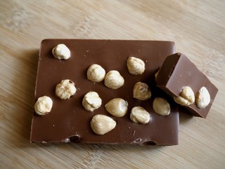 Top view photo of a chocolate bar with hazelnuts on a bamboo board surface. Milk chocolate with nuts.