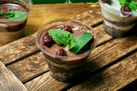 Vegetarian healthy dessert trifle with chocolate and cherry in a plastic container on a wooden background