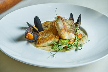 Fried pike perch fillet with cream sauce and mussels in a white bowl. Restaurant serving dishes....