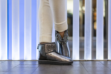 beautiful female silver uggs with rhinestones on the legs of the model in the interior. Side view. Shoe store. Festive shoes
