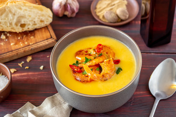 Cheese cream soup with grilled shrimp on a wooden background.