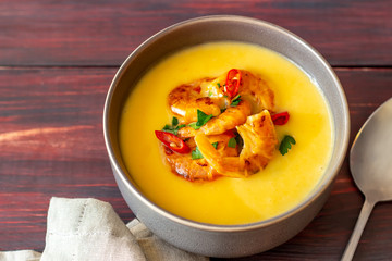 Cheese cream soup with grilled shrimp on a wooden background.