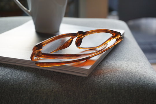 Reading glasses and a cup of coffee on a book. Cosy home interior scenery.
