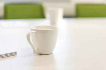 Konzept GesprÃ¤ch, Warten, Meeting: WeiÃŸe Kaffeetasse an einem weiÃŸen Tisch in einem BÃ¼ro mit Notizzetteln und StÃ¼hlen â€“ selektiver Fokus mit sehr TiefenunschÃ¤rfe, sehr viel Copyspace