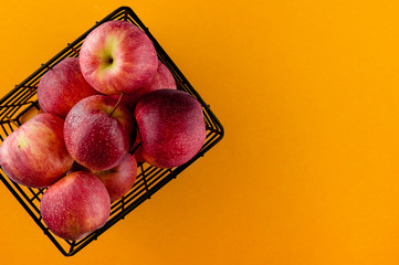Red apples in the metallic black basket on bold yellow paper background. Top view flat lay composition. Space for text template. Fresh autumn fruit wallpaper.