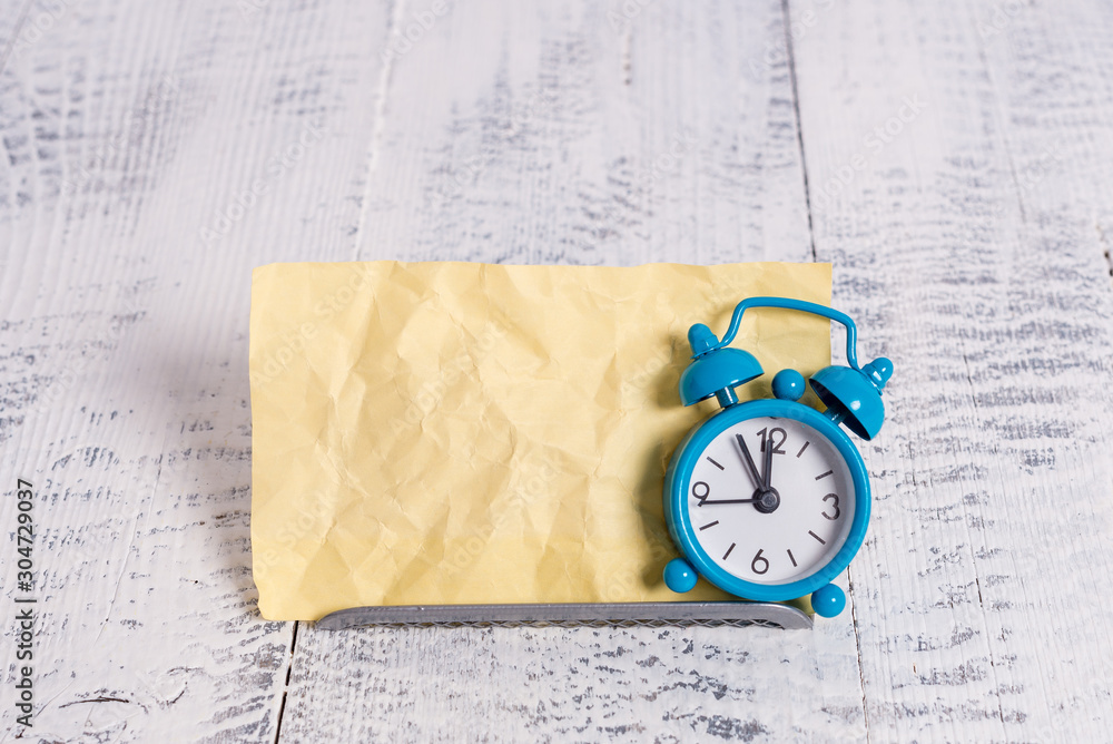 Poster mini blue alarm clock stand tilted above buffer wire in front of notepaper