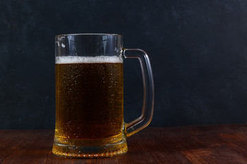 Mug of beer on wooden table on dark background