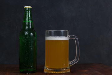 Mug of beer and green bottle with beer on wooden table on dark background