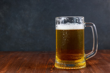 Beer in a mug with water drops on wooden table on dark background.