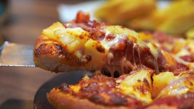 Close up metal pizza spatula taking slice of pizza in wood dish on wooden table.
