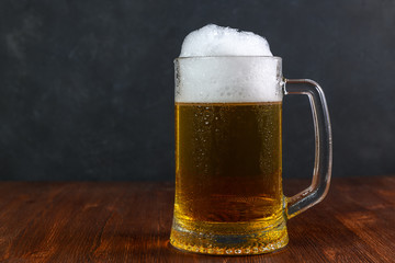 Mug of beer on wooden table on dark background