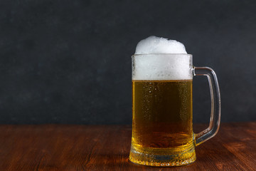 Beer in a mug with water drops on wooden table on dark background.