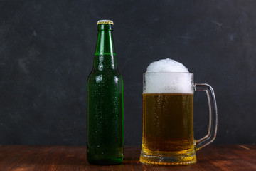 Mug of beer and green bottle with beer on wooden table on dark background