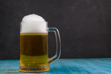 Beer in a mug with water drops on wooden table on dark background.