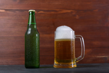 Mug of beer and green bottle with beer on wooden table on dark background