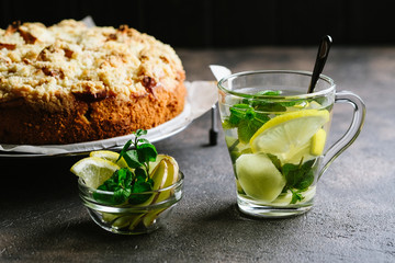Fresh ginger tea with lemon slices, mint  and hommade apple pie on a dark background.