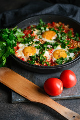 Traditional  shakshuka with eggs, tomato, and parsley in a iron pan on a dark background