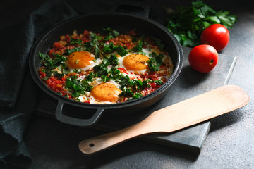 Traditional  shakshuka with eggs, tomato, and parsley in a iron pan on a dark background