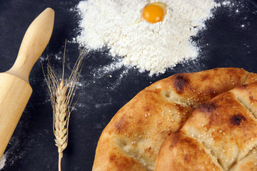 Two pita breads with a golden crust lie on a table next to flour, an egg and a rolling pin