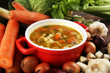 Broth with noodles and carrots, various fresh vegetables in a pot - colorful fresh clear spring soup. Rural kitchen scenery vegetarian bouillon stock