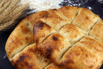 Two pita breads with a golden crust and sesame seeds lie on a table with flour