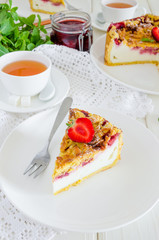 Baked creamy cheesecake with strawberries and crispy shtrezel on a plate on a white wooden background with a cup of tea.