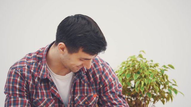 Young attractive man is sitting, taking keys to his apartment, extending them to the camera, smiling, selling his flat and moving out.