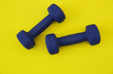 blue dumbbells isolated on a yellow background. The concept of fitness, gym and healthy lifestyle. Top view. Flat lay. Copy space for text. Background, pattern, banner.