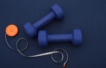 Obraz na płótnie Canvas blue dumbbells with tape measure on a blue background. The concept of fitness, gym and healthy lifestyle. Fighting overweight. Flat lay. Top view. Copy space. Background, pattern, banner.