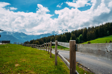 Fototapeta na wymiar Vintage fence and countryside road in Swiss Alps. Summer green rural farm landscape.