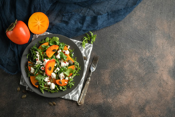 Healthy salad with persimmons, arugula, feta cheese and pumpkin seeds on a dark plate on a dark background. Vegetarian menu, healthy food. Prevention of vitamin deficiency. Top view.