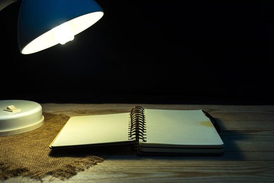A notebook placed on a table with a lamp for reading  With a black background