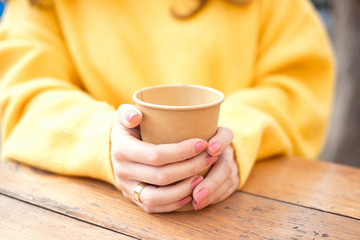 Girl's hand holding a cup of kraft paper hot coffee in a cafe on the street.