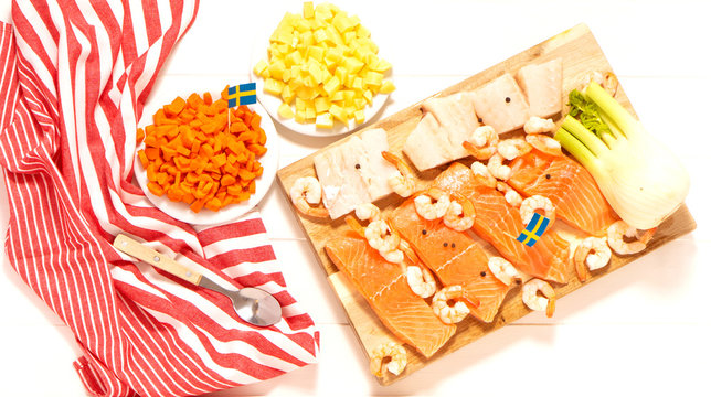 Salmon, Cod, Fennel On A Wooden Cutting Board. Potatoes And Carrots In White Plates. Spoon And Striped Tablecloth. Swedish Flags. Ingredients For Traditional Scandinavian Fish Soup. Swedish Food.