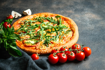 Traditional Italian pizza with ham, arugula, mozzarella, basil and tomatoes on a dark background copy space.