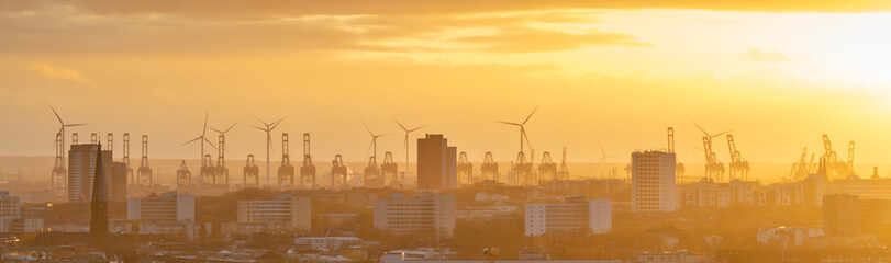 Cranes and wind turbines during sunset in the harbor area of Hamburg, Germany.