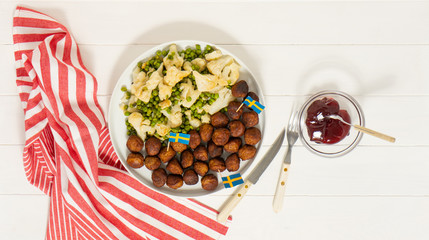 Traditional swedish meatballs (kottbullar) with cauliflower and green peas, brown sauce in the white plate. Swedish flags. Swedish national food concept. Background photo. top view.