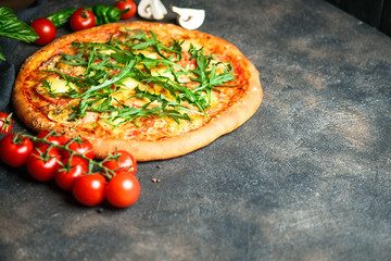 Traditional Italian pizza with ham, arugula, mozzarella, basil and tomatoes on a dark background copy space.