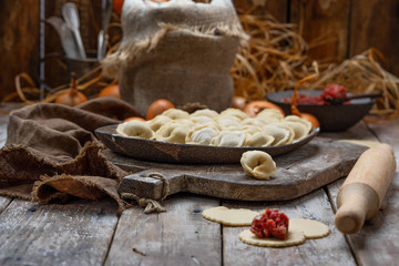 uncooked meat dumplings - russian pelmeni on cutting board and ingredients for homemade pelmeni on wooden table. Process of making pelmeni, ravioli or dumplings with meat