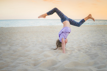 Child plays sports on the sea beach. Babe doing strength training in the sand. Young gymnast girl...