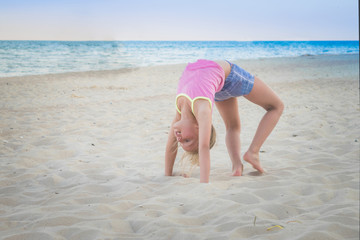 Child plays sports on the sea beach. Babe doing strength training in the sand. Young gymnast girl...