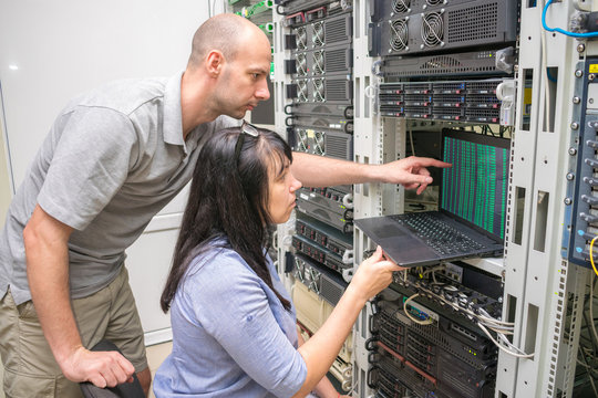  A team of experts working near the computer racks datacenter.  Teamwork concept in the field of information technology. Man and woman set up network equipment in the server room.