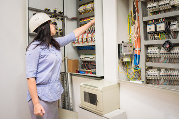 Female engineer in white helmet switches on circuit breakers in electrical box. Professional girl...
