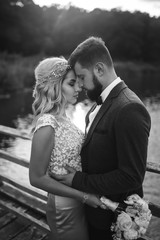 Black and white foto stylish couple of newlyweds posing on a bridge on wedding day. Handsome bearded groom admires and kisses pretty bride. Together. The concept of youth, love, fashion and lifestyle.