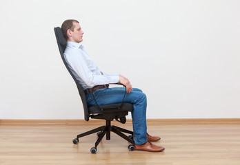 caucasian man sitting on  the edge of office chair in relaxed position