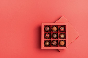 Chocolate candies in a red craft box on a bright coral background. Flat layout . Holiday Concept