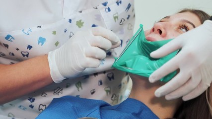 A dentist in white latex gloves makes a green rubber dam with a metal frame. Beginning of a treatment procedure in a dental clinic.