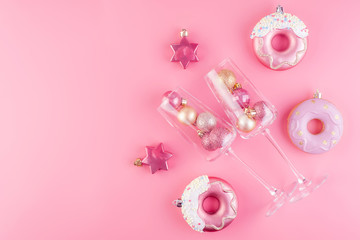 Two glasses of champagne filled with pink and gold shiny decorations on a pink pastel background.