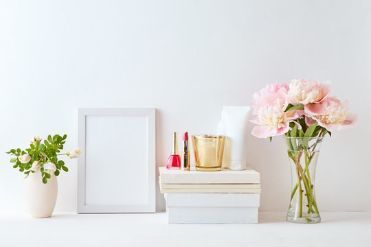 Home interior with decor elements. White frame, pink peonies in a vase, cosmetic set