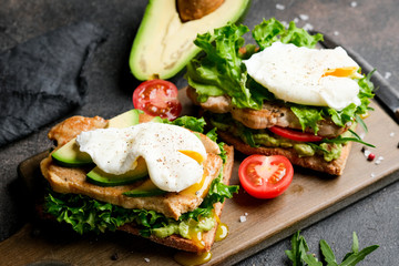 Delicious sandwich with avocado and poached egg, cherry tomatos and arugula on a dark background.
